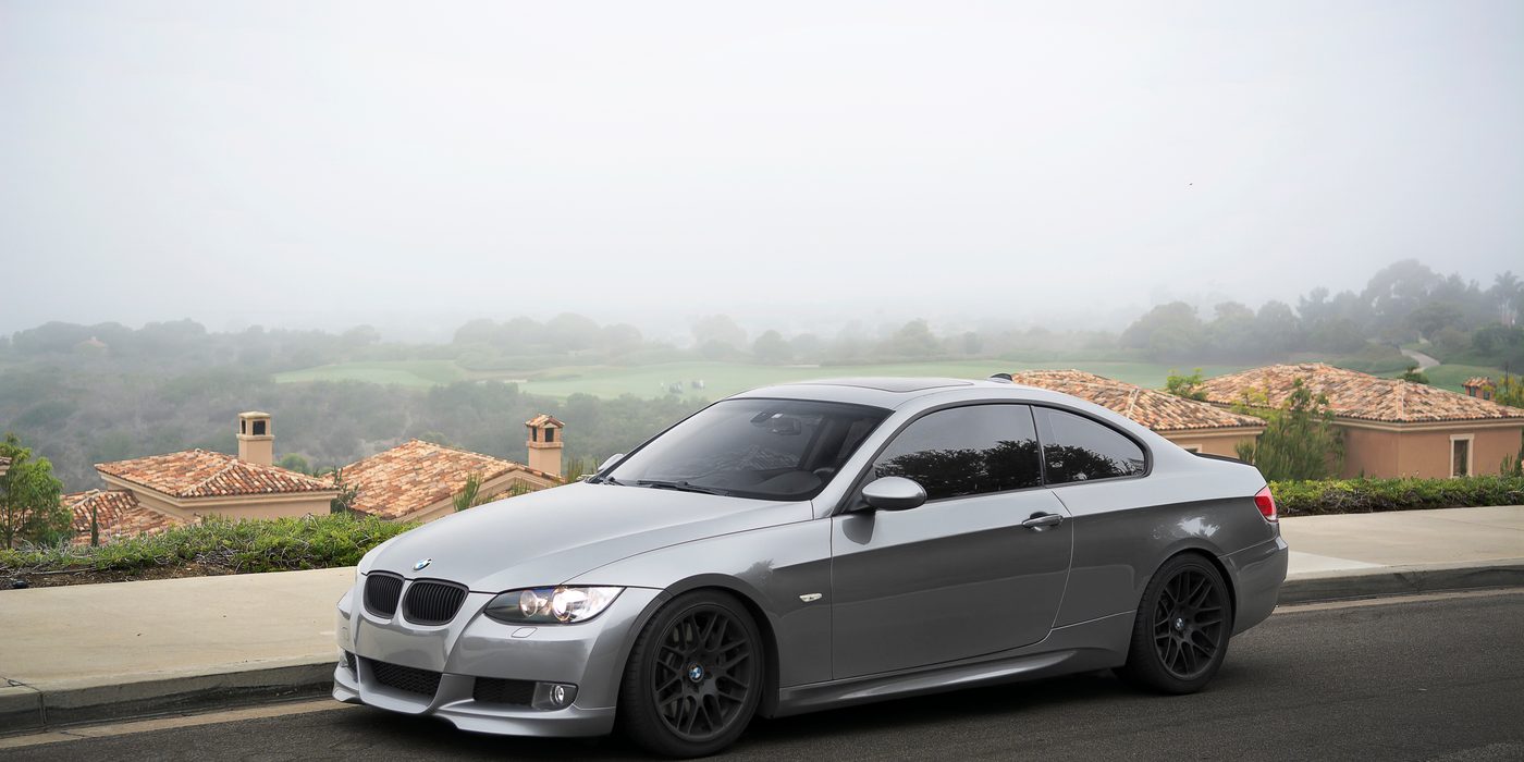 Charcoal gray BMW E90 335i sedan fitted with black VMR aftermarket wheels, parked outdoors showing aggressive stance