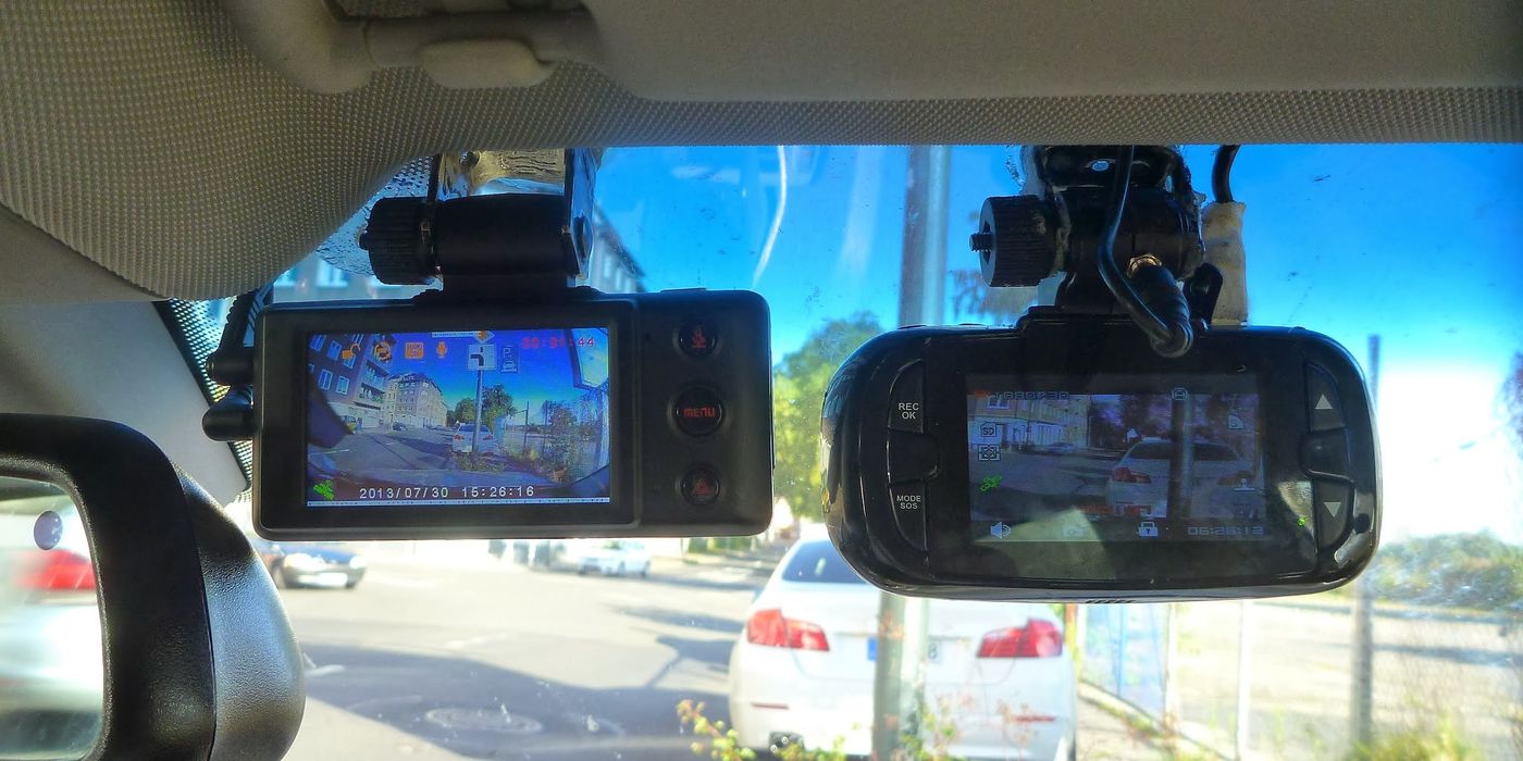 Two dashcam devices shown with suction and adhesive mounts ready for windshield installation behind the rearview mirror