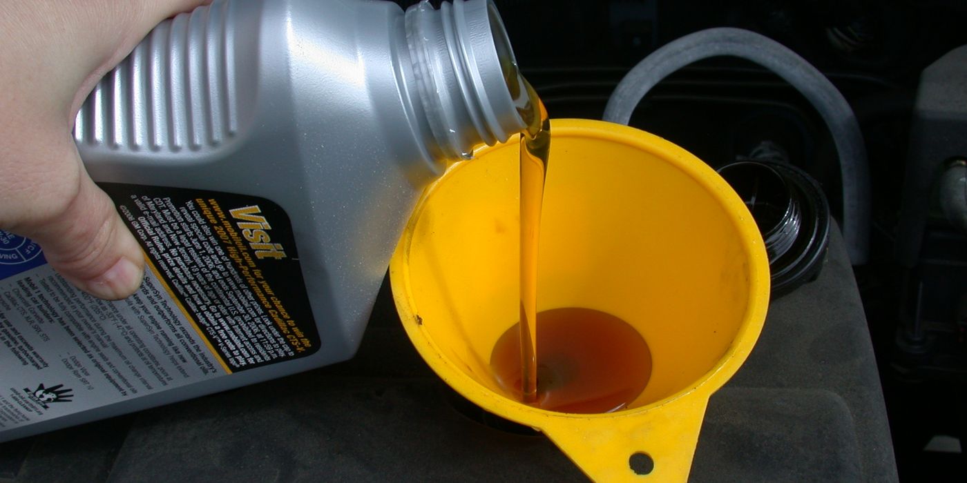 Fresh motor oil being poured through a funnel into a BMW engine