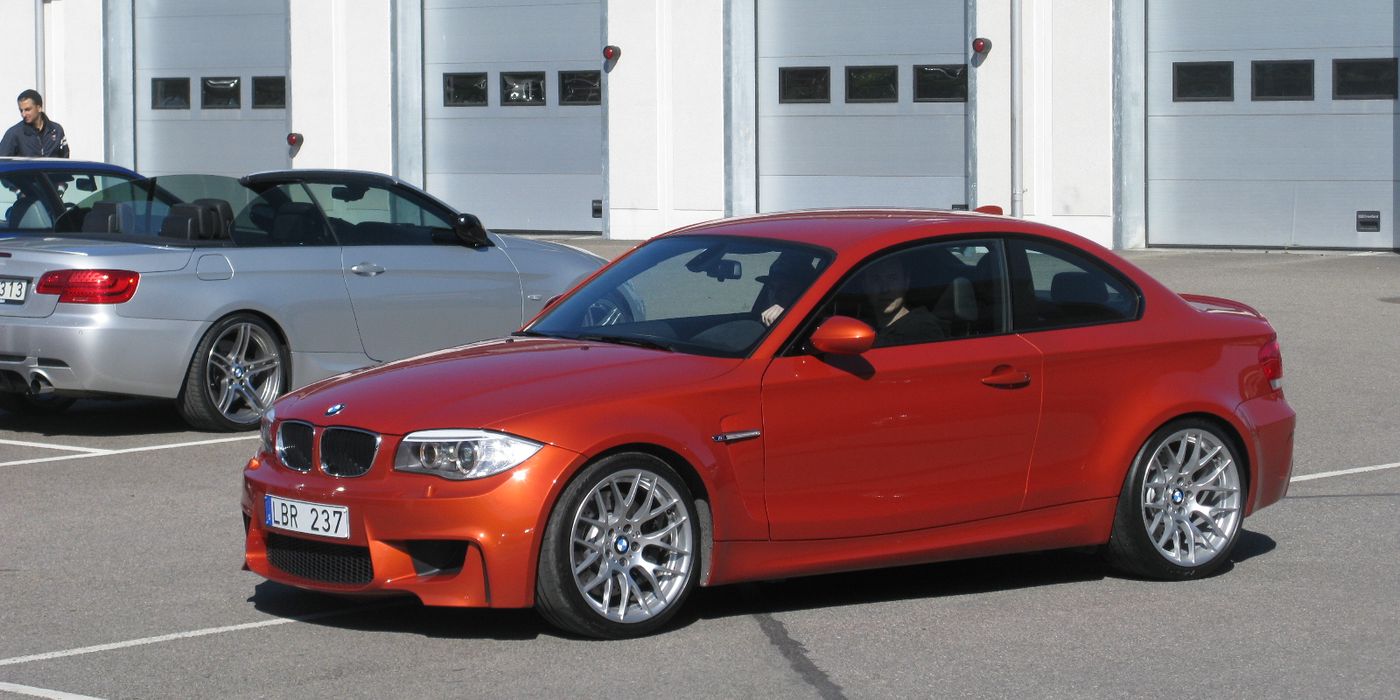 BMW 1 Series M Coupe in orange parked showing aggressive front fenders and quad exhaust
