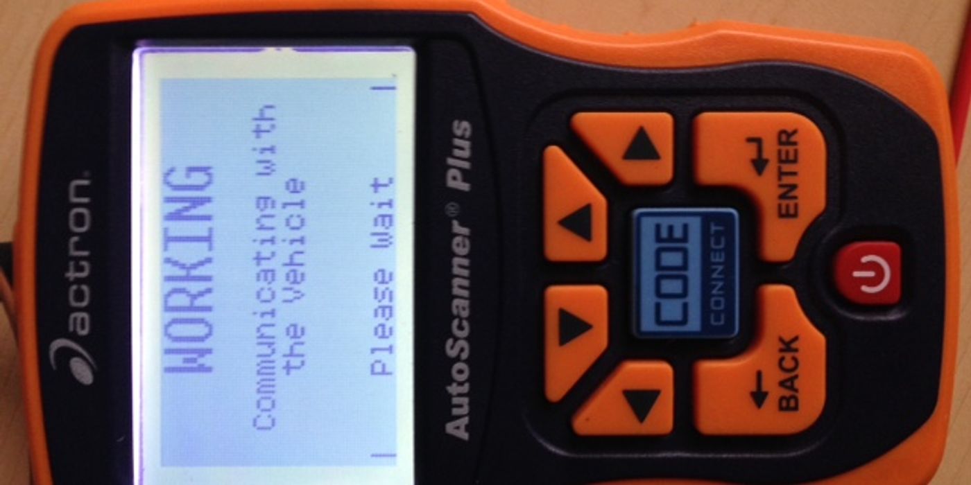 Handheld OBD-II auto scanner plugged into a car OBD port, connecting to the ECU to read diagnostic trouble codes