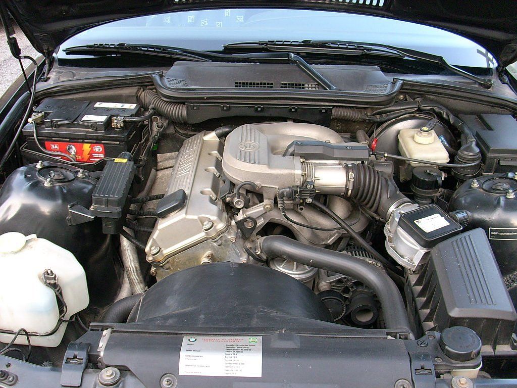 BMW E36 inline-six engine bay showing the coolant expansion tank, radiator, hoses and fan shroud at the front of the bay