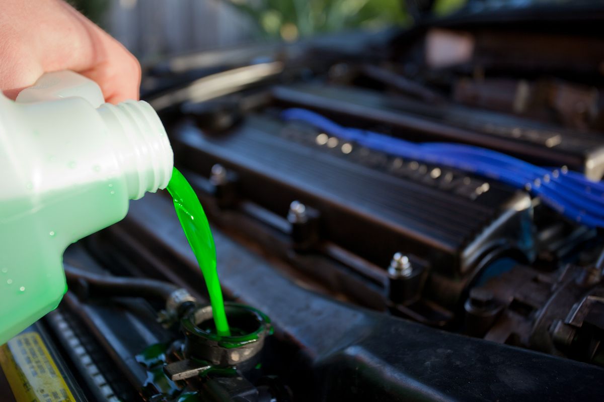 Bottle of engine coolant being poured into a vehicle cooling system at the expansion tank or radiator filler neck